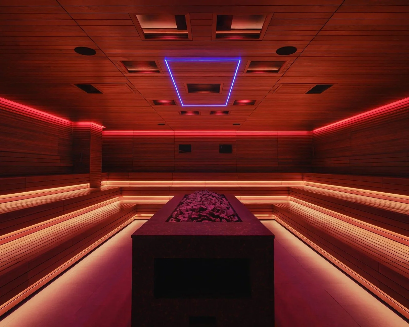 Bathhouse Philadelphia event sauna with a long stone island heater, tiered timber benches and red ceiling lighting