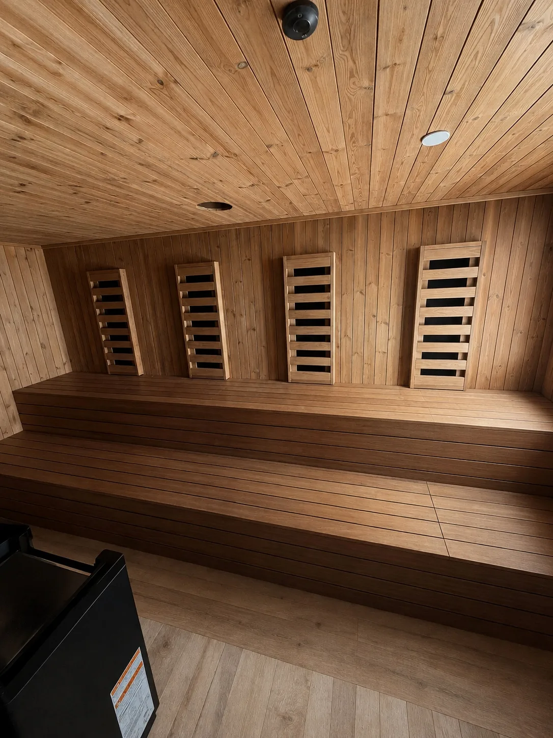 AIRE Ancient Baths sauna interior at installation stage: two timber bench tiers, four timber infrared-panel guards and an unfinished round ceiling opening