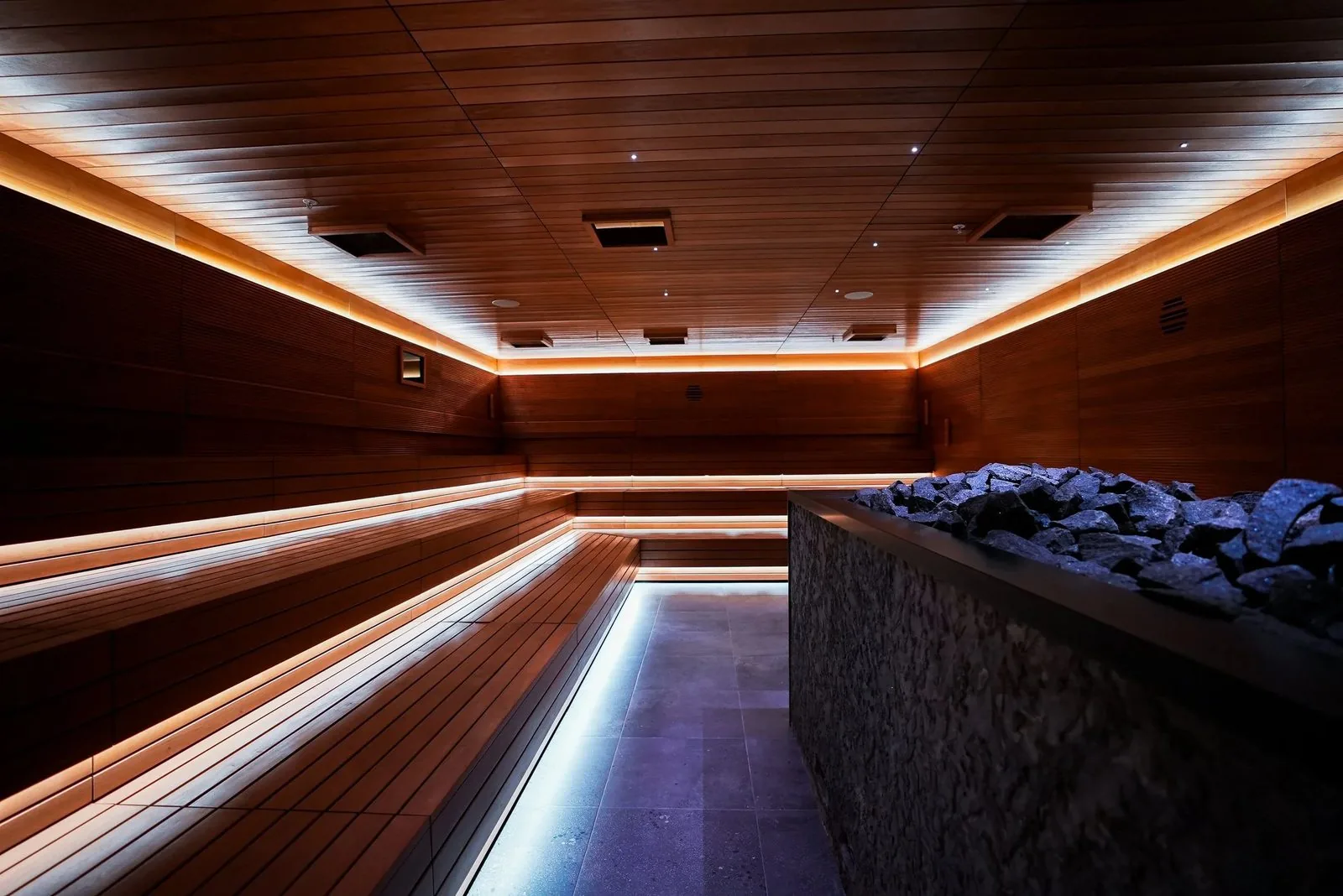 Bathhouse Atlantic event sauna: tiered timber benches with lit edges, a stone-clad heater and a lit floor channel